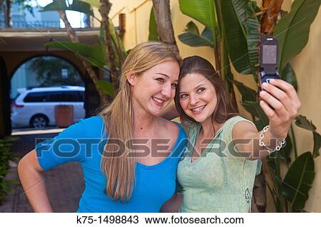 Stock Image - Two friends taking self portrait with camera phone. Fotosearch