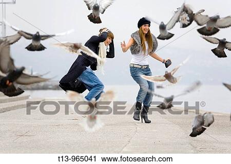 Two girlfriends and a flock of pigeons taking off View Large Photo Image Stock Image - Two girlfriends and a flock of pigeons taking off. Fotosearch