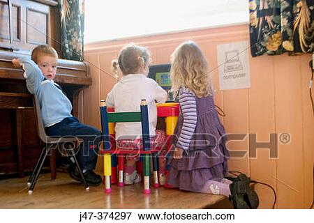 Two girls and a boy sitting at a desk looking at the computer View Large Photo Image Stock Photo - Two girls and a boy sitting at a desk looking at the computer. Fotosearch