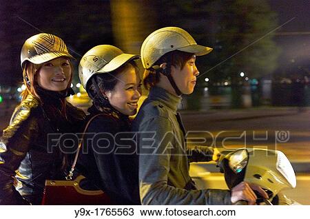 Two girls and a young man crammed on one scooter on the streets of Vietnam at night View Large Photo Image Stock Image - Two girls and a young man crammed on one scooter on the streets of Vietnam at night. Fotosearch