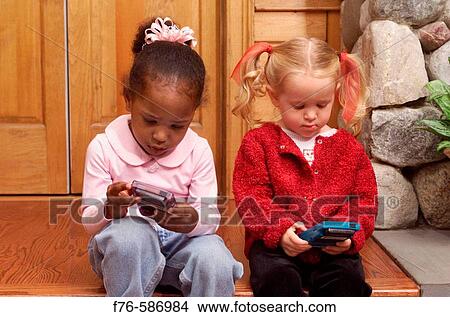 Two girls intently playing hand held computer games. View Large Photo Image Picture - Two girls intently playing hand held computer games.. Fotosearch