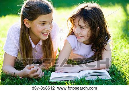 Stock Image - Two girls laughing in the garden while reading a book. Fotosearch