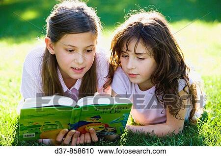 Two girls reading a book laying on the grass View Large Photo Image Stock Image - Two girls reading a book laying on the grass. Fotosearch