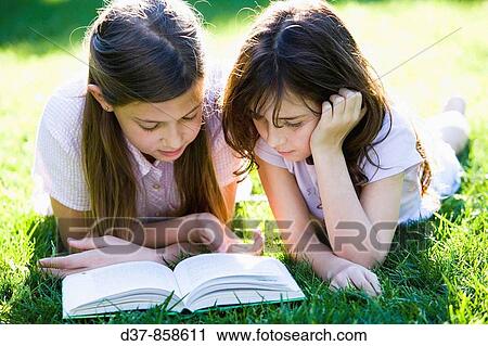 Two girls reading a book laying on the grass View Large Photo Image Stock Image - Two girls reading a book laying on the grass. Fotosearch