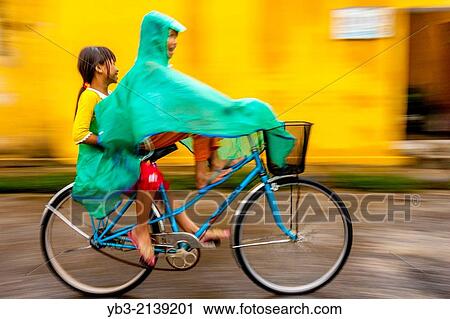 Two Girls Riding A Bike In The Rain, Hoi An, Vietnam. View Large Photo Image Stock Image - Two Girls Riding A Bike In The Rain, Hoi An, Vietnam.. Fotosearch
