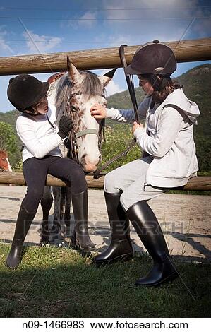 Stock Image - two girls takes care of his horse. Fotosearch