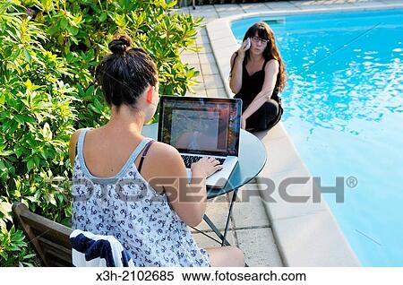 two girls using a laptop computer and a cellphone beside a swimming pool, Ile de France region, France, Europe. View Large Photo Image Stock Photography - two girls using a laptop computer and a cellphone beside a swimming pool, Ile de France region, France, Europe.. Fotosearch