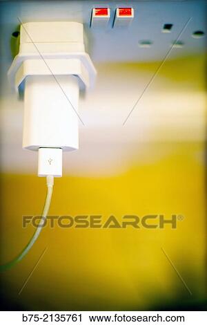 Stock Image - Two hands of electricity in position ON and mobile phone charger with UK adapter connected to the mains in England.. Fotosearch