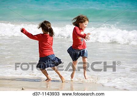 Stock Image - Two happy girls jumping by the sea having fun. Fotosearch