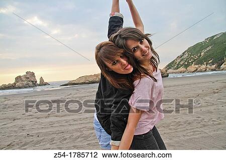 Stock Image - Two happy young women at El Sabl? n beach, Asturias, Spain. Fotosearch