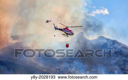 Stock Image - Two helicopters hauling water buckets to fight fire, South Jordan, Utah, USA. Fotosearch