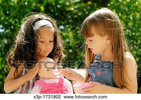 Two little girls feeding a doll View Large Photo Image Stock Image - Two little girls feeding a doll. Fotosearch