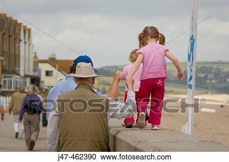 Two little girls walking along a wall, with their daddy and grandad holding hands View Large Photo Image Stock Image - Two little girls walking along a wall, with their daddy and grandad holding hands. Fotosearch