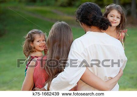 Two little sisters looking over the shoulders of their parents View Large Photo Image Stock Photo - Two little sisters looking over the shoulders of their parents. Fotosearch