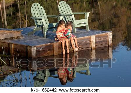 Two little sisters sitting on dock with their feet in the water View Large Photo Image Stock Image - Two little sisters sitting on dock with their feet in the water. Fotosearch