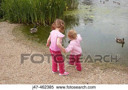 Two lttle girls feeding the ducks by a lake View Large Photo Image Stock Photography - Two lttle girls feeding the ducks by a lake. Fotosearch