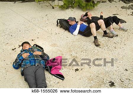 Stock Photograph - two men and a woman relax on a beach on Saltspring Island, BC, Canada. Fotosearch