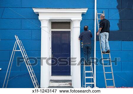 Stock Photo - Two men on ladders painting a house blue, UK. Fotosearch
