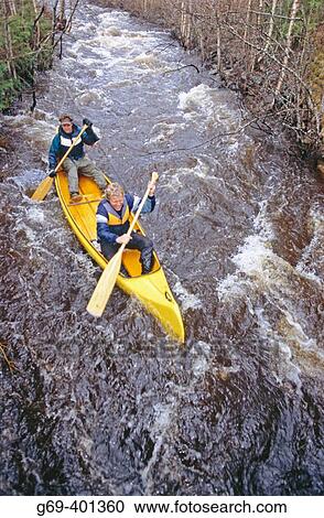 Stock Image - Two men paddling a canoe in a streamy river in spring. Klintforsliden, Vasterbotten. Sweden.. Fotosearch