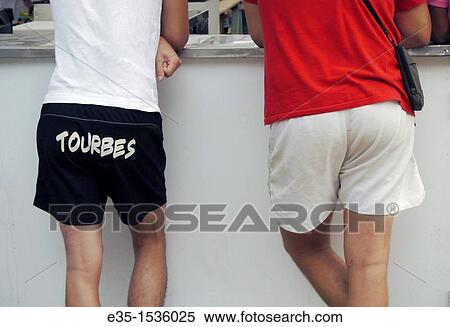 Stock Photography - Two men relax at a bar, one has the name of his town written across his shorts. Fotosearch