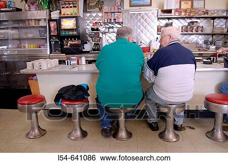 Two men sit at the counter in a small diner to eat View Large Photo Image Stock Photograph - Two men sit at the counter in a small diner to eat. Fotosearch