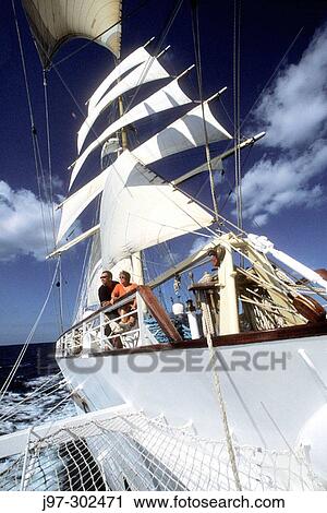 Stock Image - Two passengers leaning by the starboard rail and enjoying the sail as the clipper ship? Star Clipper? sails along the Yucatan coast towards Honduras. Fotosearch