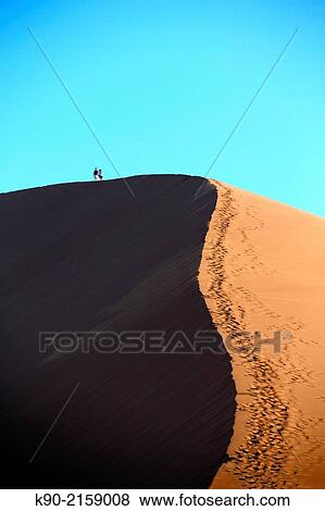 Two people are up on the top of the sand dunes in the sun, with shadow, Sossusvlei, Namib-Naukluft Park, Namibia, Africa. View Large Photo Image Stock Photo - Two people are up on the top of the sand dunes in the sun, with shadow, Sossusvlei, Namib-Naukluft Park, Namibia, Africa.. Fotosearch