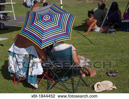 two people in camping chairs from behind in a park at a concert with a striped sun umbrella. View Large Photo Image Stock Image - two people in camping chairs from behind in a park at a concert with a striped sun umbrella.. Fotosearch