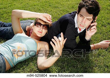 Picture - Two people on grass using palm pilot and cell phone. Fotosearch