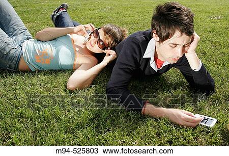 Stock Image - Two people on grass using palm pilot and cell phone. Fotosearch