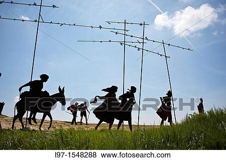 Stock Photo - Two pilgrims walk past metal sculpture silhouettes of pilgrims on the Camino de Santiago, near Pamplona, Spain. Fotosearch