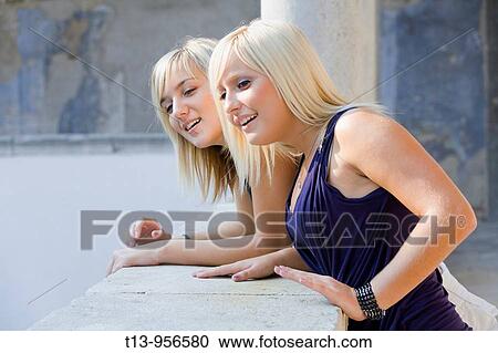 Two pretty girls are looking downwards from a balcony View Large Photo Image Stock Image - Two pretty girls are looking downwards from a balcony. Fotosearch