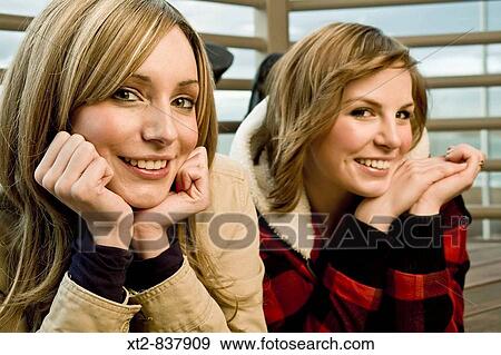 Two pretty young women rest their chins in their hands and smile for the camera View Large Photo Image Stock Photo - Two pretty young women rest their chins in their hands and smile for the camera. Fotosearch