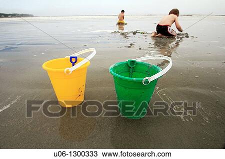 two sand pails at a beach with two children playing in the sand behind them View Large Photo Image Stock Image - two sand pails at a beach with two children playing in the sand behind them. Fotosearch