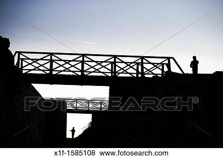 Stock Photo - Two seperate people standing, and footbridges, silhouetted at dusk, UK. Fotosearch