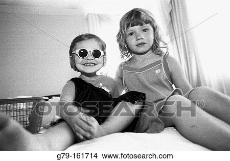 Picture - Two sisters sitting on edge of bed. Fotosearch