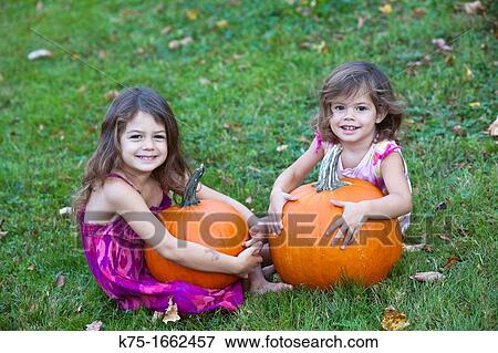 Two sisters sitting on lawn holding pumpkins View Large Photo Image Stock Photo - Two sisters sitting on lawn holding pumpkins. Fotosearch