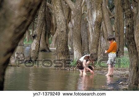 Two small children playing at the edge of a pond in a forest of trees View Large Photo Image Stock Photo - Two small children playing at the edge of a pond in a forest of trees. Fotosearch