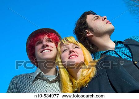 Stock Photo - Two teen boys, one with dyed red hair, and a blond teen girl standing together outside and looking around. Fotosearch