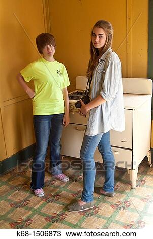 Stock Image - two teen girls stand in teh kitchen of an abandoned house. Fotosearch