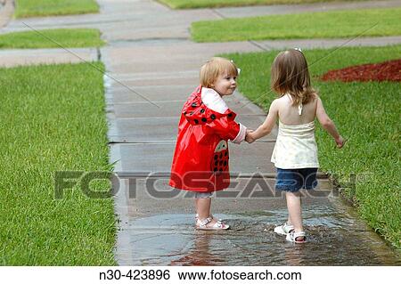 Two toddlers holding hands walking through puddle View Large Photo Image Stock Photograph - Two toddlers holding hands walking through puddle. Fotosearch