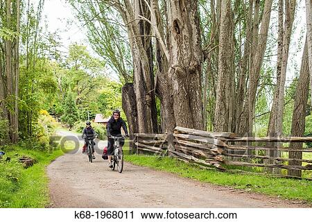 Stock Image - Two women, 27 and 40, bicycling on Saturna Island, Gulf Islands, BC, Canada.. Fotosearch