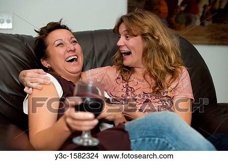 Two women enjoying wine, laughing and having fun while sitting on a sofa View Large Photo Image Picture - Two women enjoying wine, laughing and having fun while sitting on a sofa. Fotosearch