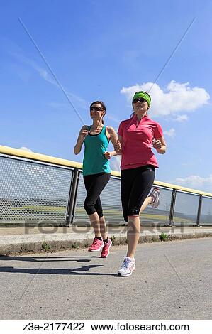 Stock Image - two women jogging over a bridge at the springtime.. Fotosearch