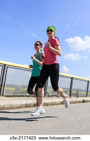 Stock Image - two women jogging over a bridge at the springtime.. Fotosearch