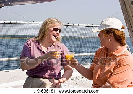 Stock Image - Two women on a? girls day out? toasting with Mimosas (champagne & orange juice) on a catamaran outside Newburyport, MA, on a September afternoon. USA. Fotosearch