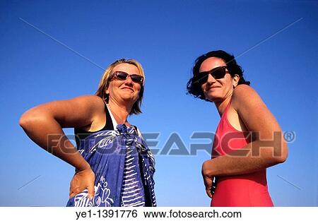 Two women standing against a blue summer sky in their swimsuits View Large Photo Image Stock Photograph - Two women standing against a blue summer sky in their swimsuits. Fotosearch