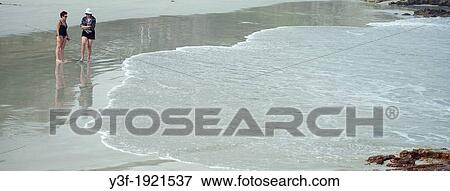 Stock Photo - Two women stroll on the beach at the edge of an incoming tide. Fotosearch