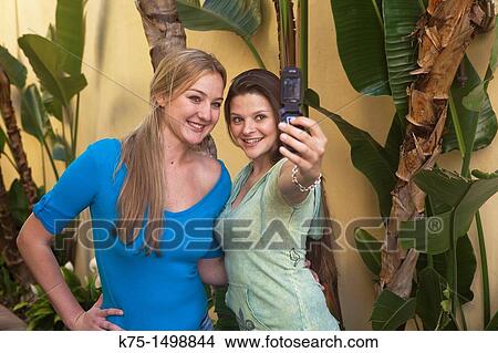 Picture - Two women taking self portrait with cell phone camera. Fotosearch