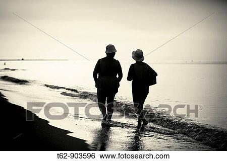 Two women walking along the seashore Vacation days Backlit View Large Photo Image Stock Photograph - Two women walking along the seashore Vacation days Backlit. Fotosearch